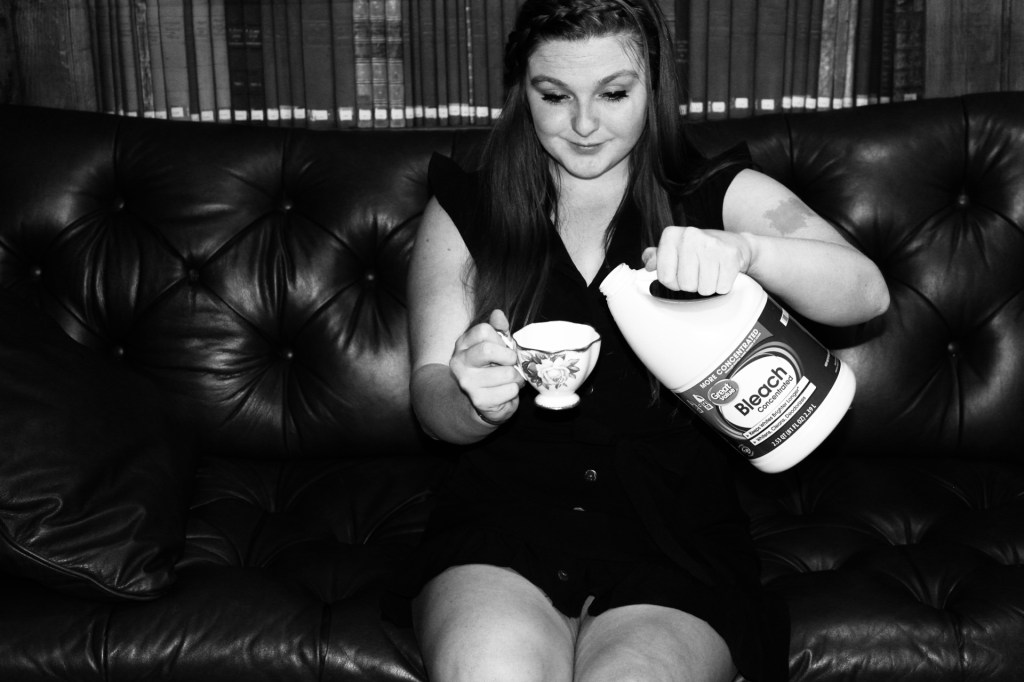 The woman sits on the leather couch. This time facing directly towards the camera but still not acknowledging the camera is there. She holds the tea cup she gave the viewer in the first frame and is filling it with bleach. She smirks as she watches her hands do the dirty work of the devil. 
