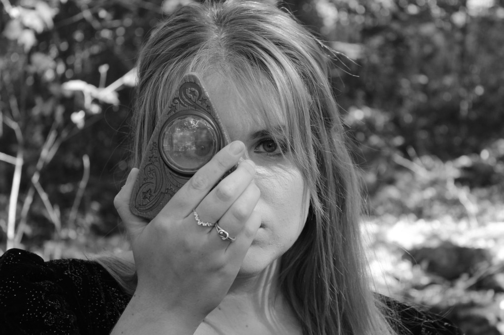 The woman holds a Oujia board Orcle to her right eye with her right hand. It enlarges her right eye while the left side of her face is exposed to the light. 