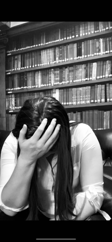 The woman sits facing the right with her hand on her head on the couch. She is crying or confessing something that has created inner turmoil in her. 